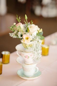 a vase filled with flowers sitting on top of a table next to cups and saucers