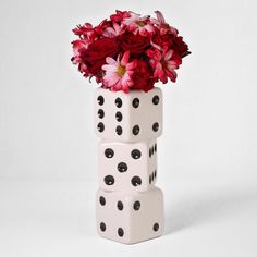 a white vase filled with red and pink flowers on top of two black polka dot dices