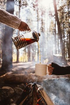 someone is pouring something into a cup over a campfire