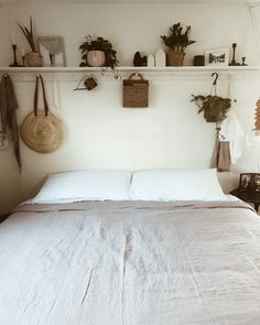 a bed with white linens and pillows in a small room filled with potted plants