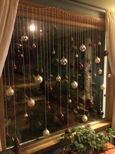 a window with christmas ornaments hanging from it's side and curtains on the outside