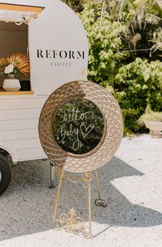 a sign that is sitting in front of a small white trailer with writing on it