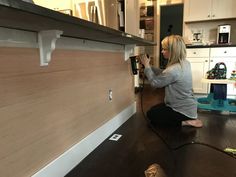 a woman is sitting on the floor working on a wood paneling wall in her kitchen