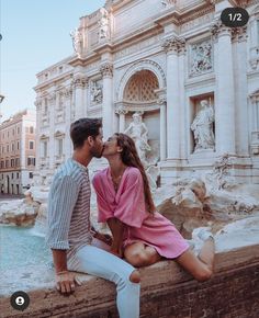 a man and woman kissing in front of a fountain