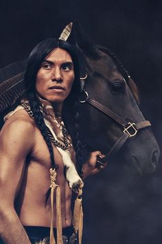 a native american man standing next to a horse in front of a dark background,