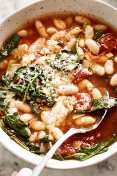 a white bowl filled with beans and spinach on top of a marble countertop