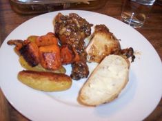 a white plate topped with different types of meats and veggies next to bread