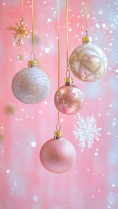 three christmas ornaments hanging from strings against a pink and white background with snowflakes