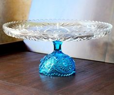 a blue glass cake plate sitting on top of a wooden table next to a bowl