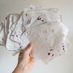 a hand holding several pieces of white paper with pink flowers on it, all over the placemats