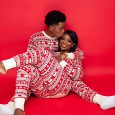 a man and woman in matching christmas pajamas pose for a photo on a red background