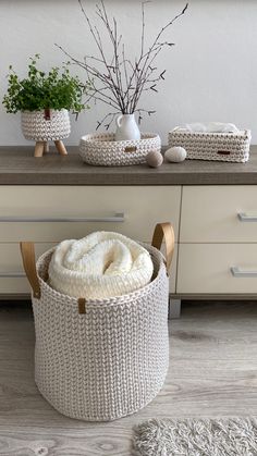 a white knitted basket sitting on top of a wooden table next to a plant