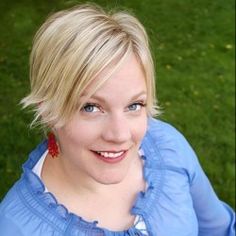 a woman with blonde hair wearing a blue shirt and smiling at the camera while standing in front of green grass