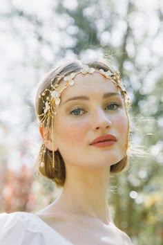 a woman wearing a gold head piece with pearls and leaves on her hair, looking off to the side