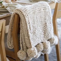 a white knitted blanket sitting on top of a wooden chair next to a table