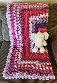 a crocheted blanket with a teddy bear sitting on top of it next to a pillow