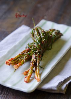 asparagus with sesame seeds and seasoning on a white plate sitting on a wooden table