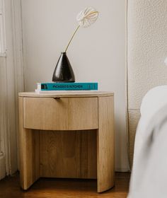 a wooden table with a book and flower on it next to a white bed in a room