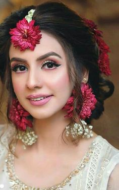 a woman with red flowers in her hair and pearls around her neck, smiling at the camera