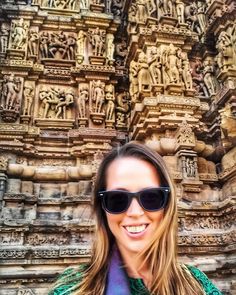 a woman wearing sunglasses standing in front of a stone structure with carvings on it's sides