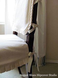 a white bed sitting next to a window in a room with curtains on the windowsill