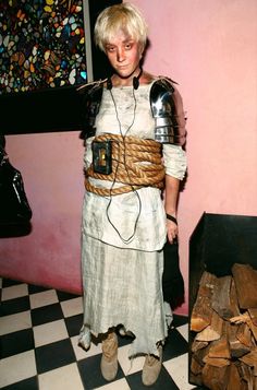 a woman dressed as a roman gladiator in front of stacks of firewood