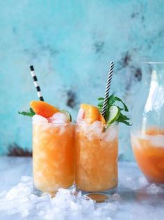 two glasses filled with orange and limeade cocktails sitting on top of snow covered ground