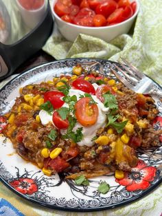 a white plate topped with meat and veggies next to a bowl of tomatoes