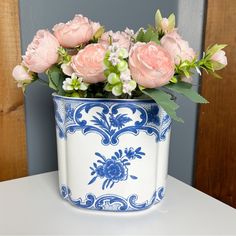 a blue and white vase with pink roses in it on a table next to a wall