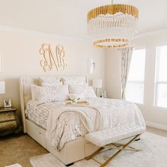 a white bedroom with a chandelier hanging from the ceiling and a large bed