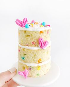 a hand holding a three layer cake with white frosting