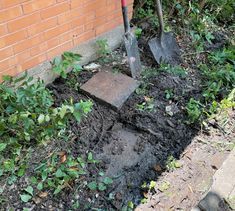 shovels are stuck in the ground next to a brick wall