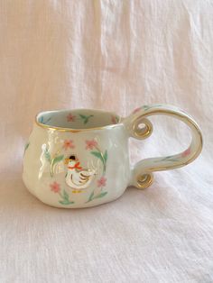 a white and gold coffee cup with a duck on the inside is sitting on a white cloth