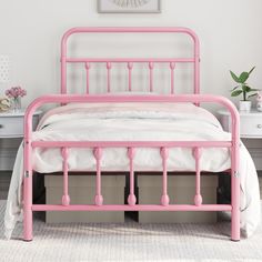 a pink metal bed with white sheets and pillows