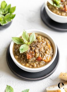 two white bowls filled with soup next to crackers and green leafy garnish