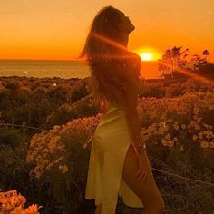 a woman standing in front of the ocean at sunset with her back to the camera