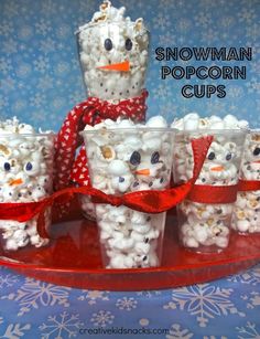 snowman popcorn cups are on a red tray and have been decorated to look like marshmallows