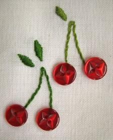 three cherries with green leaves on white linens, one red and one green