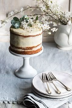 there is a cake on the table with two forks and flowers in vases behind it