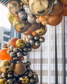 a bunch of balloons that are hanging from a ceiling in front of a window with curtains