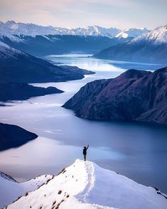 a man standing on top of a snow covered mountain next to a body of water