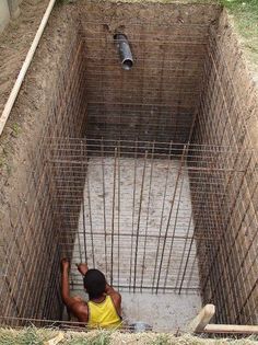 a man in yellow shirt laying on the ground next to a caged area with pipes