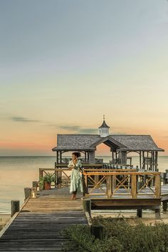 a woman standing on the end of a pier next to the ocean with a gazebo in the background