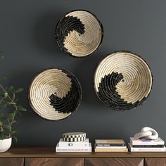 three black and white baskets mounted on the wall above a wooden table with books, plant and vase