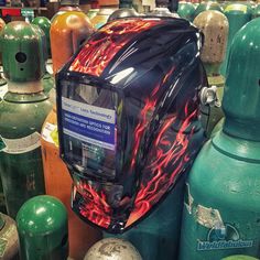 a helmet with flames on it sitting in front of other green and yellow gas cans