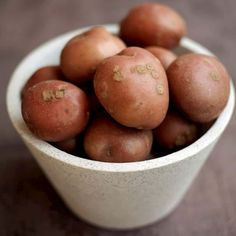 a white bowl filled with red potatoes on top of a wooden table