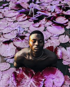 a man sitting in the middle of water surrounded by pink and purple flowers with his eyes closed