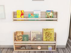 two wooden shelves with books on them against a white wall and wood flooring in front of it