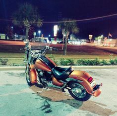 an orange and black motorcycle parked in a parking lot next to palm trees at night