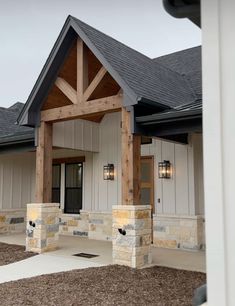 the front entrance to a home with stone pillars and wood beams on it's roof